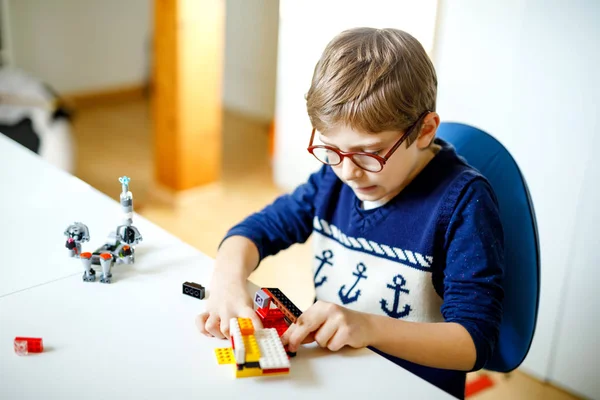 Маленький блондин в очках играет с большим количеством красочных пластиковых блоков. Очаровательный школьник развлекается со строительством и созданием робота. Творческий досуг современная техника и робототехника. — стоковое фото