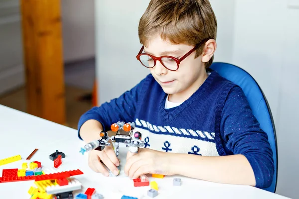 Kis szőke gyermek szemüveg játszik sok színes műanyag blokkok. Imádnivaló iskolás fiú szórakozik a robot építésével és létrehozásával. Kreatív szabadidő modern technika és robot. — Stock Fotó