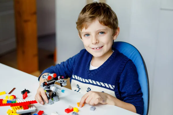 Renkli plastik bloklar çok oynayan küçük sarışın çocuk. Sevimli okul çocuk çocuk bina ve robot oluşturma ile eğlenmek. Yaratıcı eğlence modern teknik ve robotik. — Stok fotoğraf