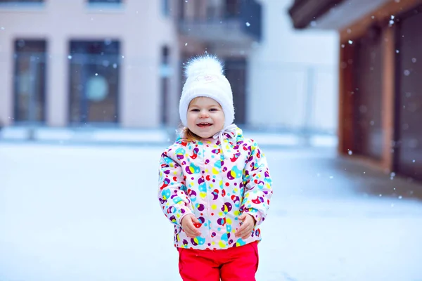 Ritratto di bambina che cammina all'aperto in inverno. Carino il bambino che mangia dolci caramelle lecca lecca. Bambino che si diverte nella fredda giornata sulla neve. Indossare vestiti caldi colorati bambino e cappello con ciambelle. — Foto Stock