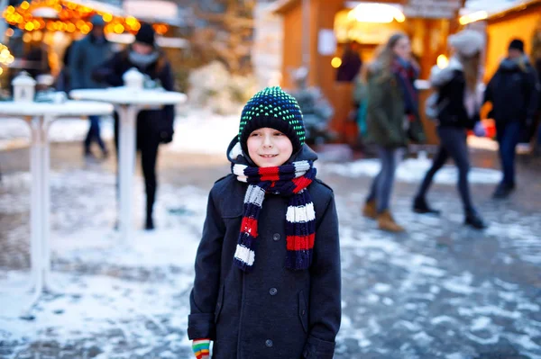 Kleine schattige jongen jongen plezier op Duitse kerstmarkt. Gelukkig kind op traditionele familie markt in Duitsland, lachend jongen in kleurrijke winterkleren — Stockfoto