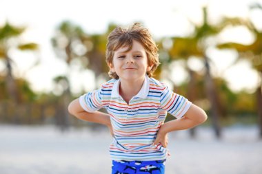 Miami sahilinde eğlenen sevimli, aktif bir çocuk, Key Biscayne. Mutlu şirin çocuk rahatlıyor, kumla oynuyor ve palmiyelerin ve okyanusun yanında güneşli bir günün tadını çıkarıyor.