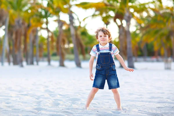 Miami sahilinde eğlenen sevimli, aktif bir çocuk, Key Biscayne. Mutlu şirin çocuk rahatlıyor, kumla oynuyor ve palmiyelerin ve okyanusun yanında güneşli bir günün tadını çıkarıyor. — Stok fotoğraf