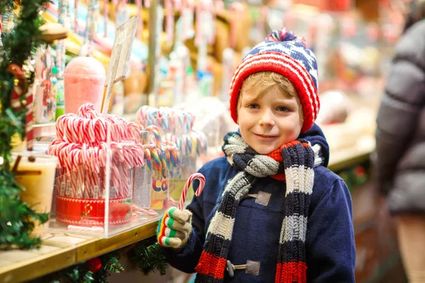 Little cute kid chłopiec zakupu słodyczy od cancy stanąć na Jarmark bożonarodzeniowy. Szczęśliwe dziecko na tradycyjnym rynku dla rodzin z dziećmi w Niemczech. Przedszkolak w kolorowe zimowe ubrania — Zdjęcie stockowe