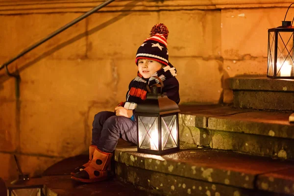 Pequeno menino bonito com uma lanterna de luz nas escadas perto da igreja. Criança feliz no mercado de Natal na Alemanha. Criança à espera dos pais no dia frio de inverno — Fotografia de Stock
