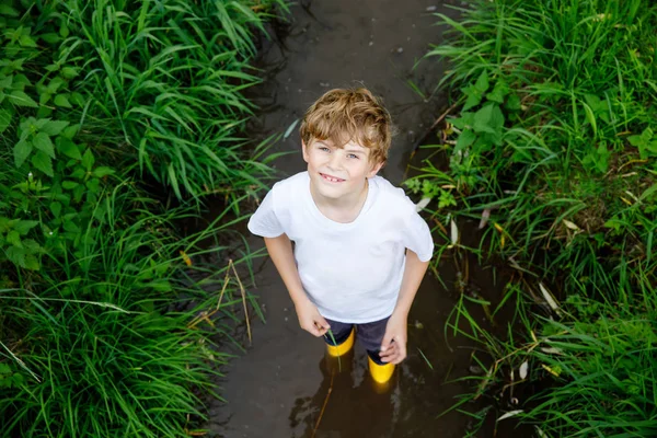 Happy little school kids boy having fun walking through water in river in gum rubber boots. child portrait of healthy kid on summer vacations, active games outdoors — Stock Photo, Image