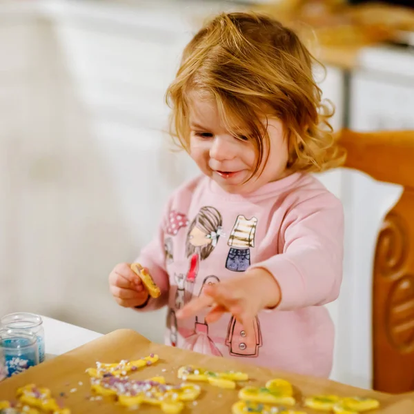 Милая маленькая девочка печет пряничное рождественское печенье дома. Очаровательный блондин, развлекающийся на домашней кухне. Традиционный отдых с детьми на Рождество. Тоддлер пробует тесто . — стоковое фото