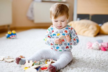 Evde ya da çocuk odasında ahşap yapboz gibi eğitici oyuncaklarla oynayan güzel bir kız bebek. Mutlu sağlıklı çocuk renkli oyuncaklarla eğleniyor. Çocuk farklı yetenekler öğreniyor