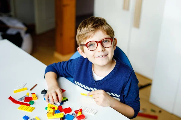 Petit enfant blond avec des lunettes jouant avec beaucoup de blocs en plastique coloré. Adorable écolier qui s'amuse avec la construction et la création de robots. Loisirs créatifs technique moderne et robotique. — Photo