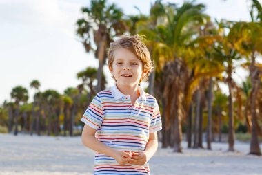 Miami sahilinde eğlenen sevimli, aktif bir çocuk, Key Biscayne. Mutlu şirin çocuk rahatlıyor, kumla oynuyor ve palmiyelerin ve okyanusun yanında güneşli bir günün tadını çıkarıyor.