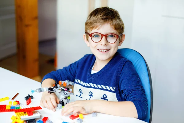 Piccolo bambino biondo con occhiali da vista che gioca con un sacco di blocchi di plastica colorati. Adorabile ragazzo della scuola divertirsi con la costruzione e la creazione di robot. Tempo libero creativo moderna tecnica e robotica. — Foto Stock