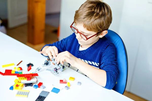 Klein blond kind met een bril spelen met veel kleurrijke plastic blokken. Schattige schooljongen die plezier heeft met het bouwen en maken van robots. Creatieve vrije tijd moderne techniek en robottechniek. — Stockfoto