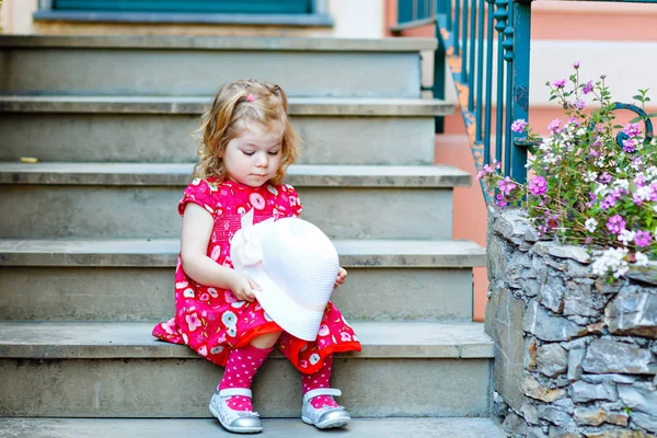 Portrét krásné malé nádherný batole dívka v růžové letní vzhled oblečení, módní šaty, kolena ponožky a klobouk. Šťastné zdravé dítě pózuje před barevným domem. — Stock fotografie