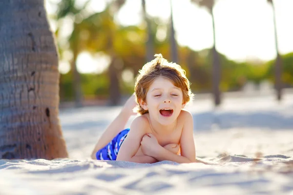 Blond adorable gorgeous little kid boy having fun on Miami beach, Key Biscayne. Happy healthy cute child playing with sand and running near ocean. Palms, security house and white sand — Stock Photo, Image