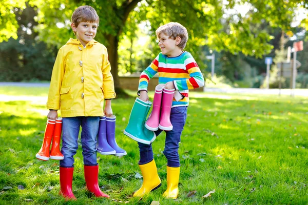 Два маленьких мальчика, симпатичные братья и сестры с кучей разноцветных сапог для дождя. Дети в разных резиновых сапогах и куртках. Обувь для дождливого падения. Здоровые близнецы и лучшие друзья веселятся на открытом воздухе — стоковое фото