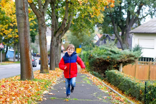 Happy little boy running on autumnal street after school. Kid happy about school vacations. Child with autumn fashion clothes wearing eye glasses — Stock Photo, Image