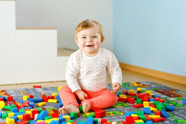 Eğitici oyuncaklarla oynayan sevimli bir kız bebek. Mutlu sağlıklı bir çocuk, evdeki renkli tahta bloklarla eğleniyor. Bebek öğrenme renkleri ve biçimleri