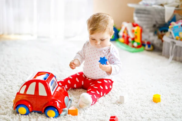 Rozkošný roztomilý krásnou holčičku hraje s vzdělávací dřevěné hračky doma nebo školky. Zdravé šťastné batole s barevné červené auto doma. dítě učení barev a forem — Stock fotografie