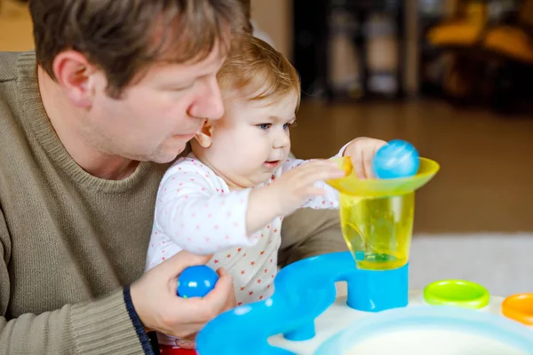 Gelukkig trotse jonge vader plezier met baby dochter, familieportret samen. Papa spelen met babymeisje met educatieve sorter speelgoed met verschillende kleurrijke ballen. Man met klein kind thuis. — Stockfoto