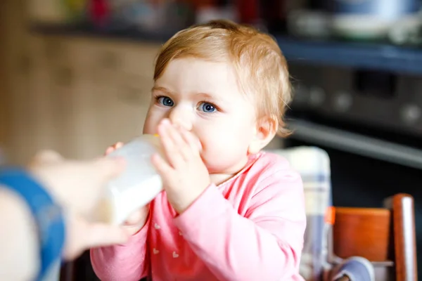 Nettes entzückendes Baby-Mädchen mit Stillflasche und trinkender Formel Milch. Erste Nahrung für Babys. Neugeborenes Kind, im Stuhl der heimischen Küche sitzend. Gesunde Babys und Flaschenfütterungskonzept — Stockfoto