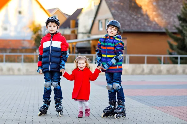 Twee kinderen jongens en meisje van de peuter samenspelen buitenshuis op een zonnige dag. Broers in bescherming veiligheid kleding schaatsen met rollen. Gelukkig zus houden van broers en zussen. Gelukkige familie van drie kinderen — Stockfoto