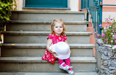 Pembe elbiseli, moda elbiseli, diz altı çoraplı ve şapkalı güzel küçük bir kız çocuğunun portresi. Renkli evin önünde poz veren mutlu sağlıklı bebek..