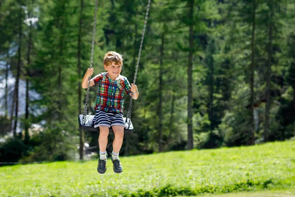 Garoto engraçado garoto se divertindo com balanço de corrente no parque infantil ao ar livre enquanto está molhado salpicado com água — Fotografia de Stock