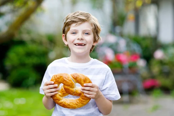 Liebenswerter kleiner Junge isst riesige große bayerische Brezel. — Stockfoto