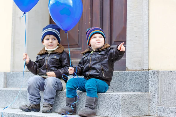 Deux petits garçons jouant avec des ballons à air bleu à l'extérieur. Joyeux jumeaux et frères tout-petits souriant et riant ensemble. Enfants en bonne santé dehors par temps froid dans des vêtements chauds . — Photo