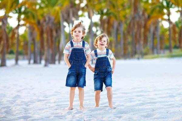 Two little kids boys having fun on tropical beach, happy best friends playing, friendship concept. Siblings brothers, twins in family look with palms on background. Family vacations on ocean. — Stock Photo, Image