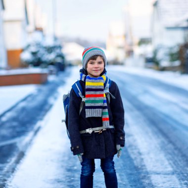 İlköğretim sınıfının küçük çocuğu kar yağarken okula yürüyor. Mutlu çocuk eğleniyor ve ilk karla oynuyor. Sırt çantalı öğrenci ya da renkli kış kıyafetleri içinde bir çanta..