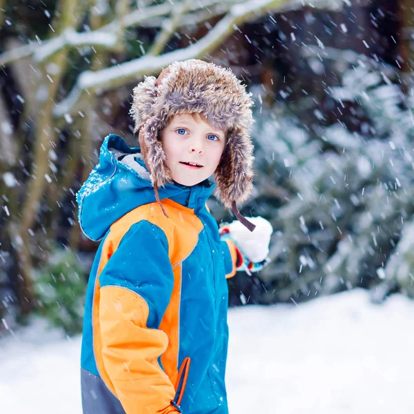 Funny little kid boy in colorful clothes playing outdoors during snowfall. Active leisure with children in winter on cold snowy days. Happy child having fun and playing with snow — Stock Photo, Image