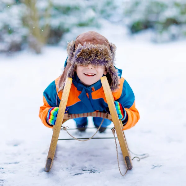 Menino da escola se divertindo com passeio de trenó durante a queda de neve. Criança feliz escorregando na neve. Um miúdo pré-escolar a andar de trenó. Criança brincando ao ar livre no parque de inverno nevado. Diversão ativa para a família — Fotografia de Stock