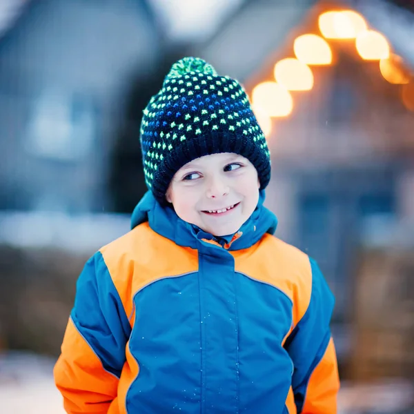 Забавный маленький мальчик в разноцветной одежде играет на улице во время снегопада. Активный отдых с детьми зимой в холодные снежные дни. Счастливый ребенок на зимних каникулах в нашей стране . — стоковое фото