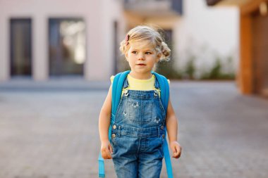 Cute little adorable toddler girl on her first day going to playschool. Healthy beautiful baby walking to nursery school and kindergarten. Happy child with backpack on the city street, outdoors. clipart