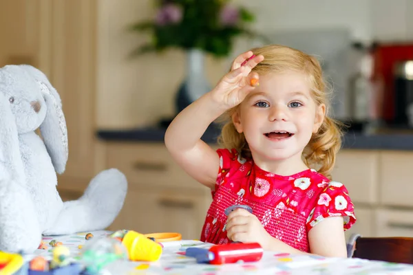 Aranyos kis aranyos kislány színes agyaggal. Egészséges baba játszik, és játékokat hoz létre játék tészta. Kis boldog vicces gyerek penész modellezés agyag, így fagylalt és etetés puha nyuszi. — Stock Fotó