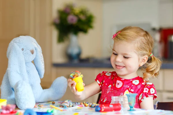 Чарівна мила маленька дівчинка з барвистою глиною. Здорова дитина грає і створює іграшки з тіста. Маленький щасливий смішний дитячий молдинг моделювання глини, виготовлення морозива та годування м'якого кролика . — стокове фото