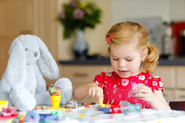 Schattige kleine peuter meisje met kleurrijke klei. Gezonde baby spelen en het maken van speelgoed van spelen deeg. Klein vrolijk grappig kind modelleren klei, het maken van ijs en het voeden van zacht konijn. — Stockfoto