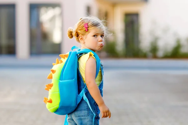 Carino piccolo adorabile bambina il suo primo giorno di andare a scuola. Sano sconvolto triste bambino a piedi alla scuola materna. Paura dell'asilo nido. Bambino infelice con zaino sulla strada della città, all'aperto — Foto Stock