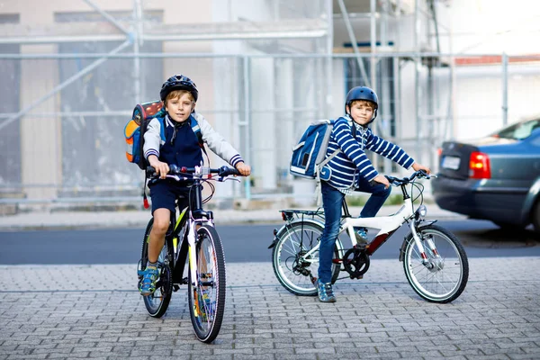 Dois meninos da escola em capacete de segurança andando de bicicleta na cidade com mochilas. Crianças felizes em roupas coloridas de bicicleta em bicicletas a caminho da escola. Maneira segura para crianças ao ar livre para a escola — Fotografia de Stock