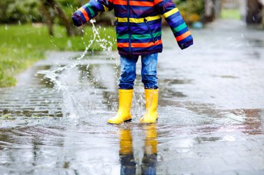 Close-up of kid wearing yellow rain boots and walking during sleet, rain and snow on cold day. Child in colorful fashion casual clothes jumping in a puddle. Having fun outdoors clipart
