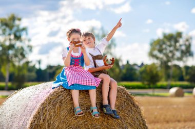 Buğday tarlasında geleneksel Bavyera kostümlü iki çocuk. Alman çocukları Ekim Festivali sırasında ekmek ve simit yiyorlar. Almanya 'da yaz aylarında erkek ve kız saman balyalarında oynuyorlar..