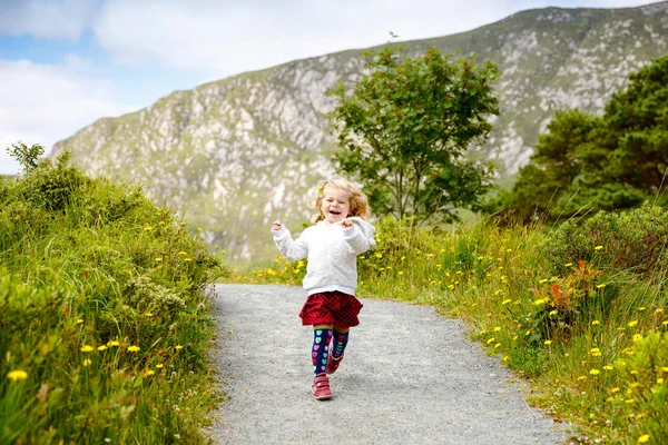 Cute little happy toddler girl running on nature path in Glenveagh national park in Ireland. Smiling and laughing baby child having fun spending family vacations in nature. Traveling with small kids — Stock Photo, Image