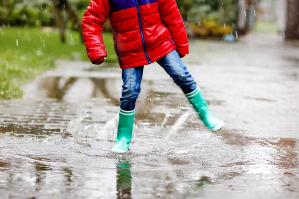 Close-up of kid wearing yellow rain boots and walking during sleet, rain and snow on cold day. Child in colorful fashion casual clothes jumping in a puddle. Having fun outdoors — Stock Photo, Image