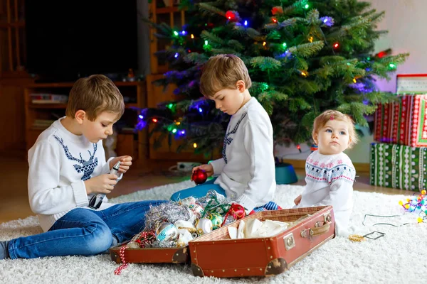 Twee kleine jongen jongens en schattige babymeisje versieren kerstboom met oude vintage speelgoed en ballen. — Stockfoto
