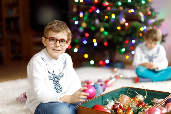 Schöner kleiner Junge mit Brille und buntem Vintage-Weihnachtsspielzeug und Bällen im alten Koffer. Kinder schmücken Weihnachtsbaum — Stockfoto