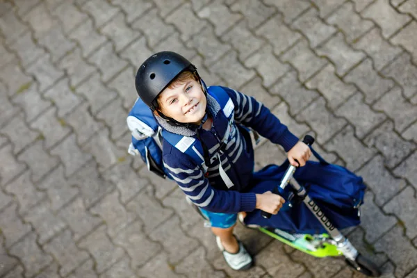 Zwei Schulkinder mit Schutzhelm fahren an einem sonnigen Tag mit dem Roller in der Stadt mit dem Rucksack. fröhliche Kinder in bunten Kleidern auf dem Schulweg. Gesichter von oben nicht wiederzuerkennen — Stockfoto