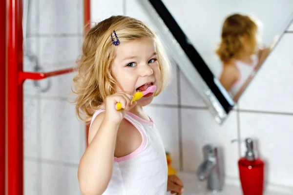 Linda niña adorable niño sosteniendo cepillo de dientes y cepillarse los primeros dientes en el baño después de dormir. Precioso bebé aprendiendo a limpiar los dientes de leche. Rutina de higiene saludable para niños — Foto de Stock