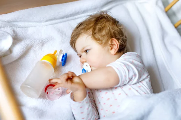 Roztomilé holčička drží láhev s vzorcem mírné a pití. Dítě v postýlce před spaním — Stock fotografie