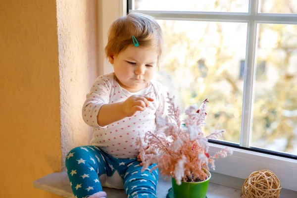Joyeux adorable petite fille mignonne assise près de la fenêtre et regardant dehors sur la neige le jour de l'hiver ou du printemps — Photo